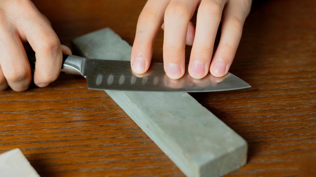 young man sharpening a knive on wooden table on dark background